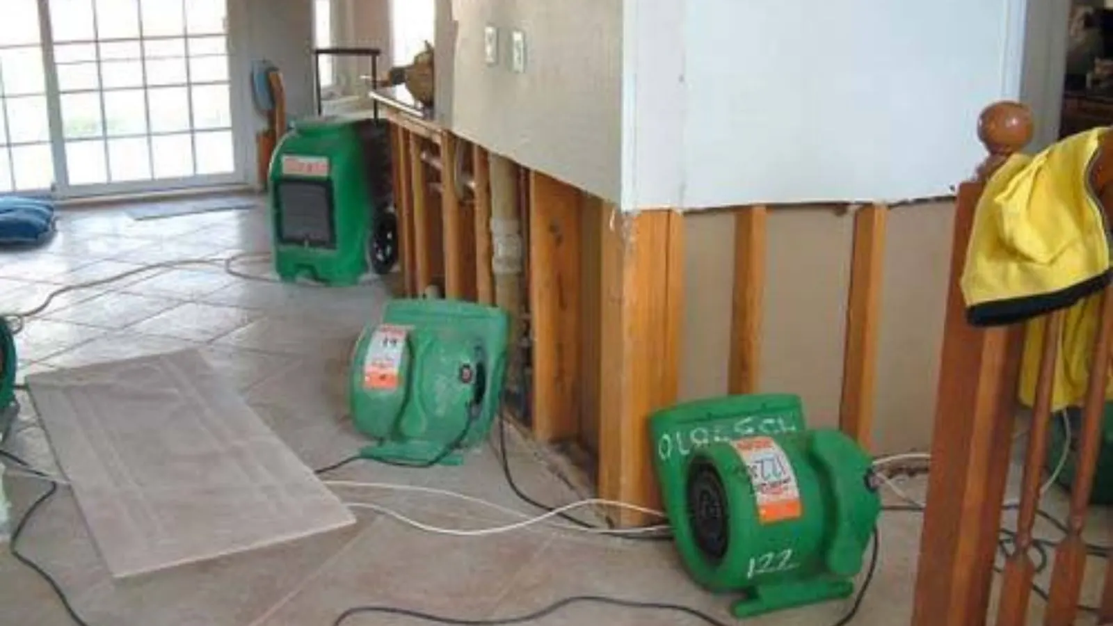 Green air movers drying a room with opened wall cavities after water damage